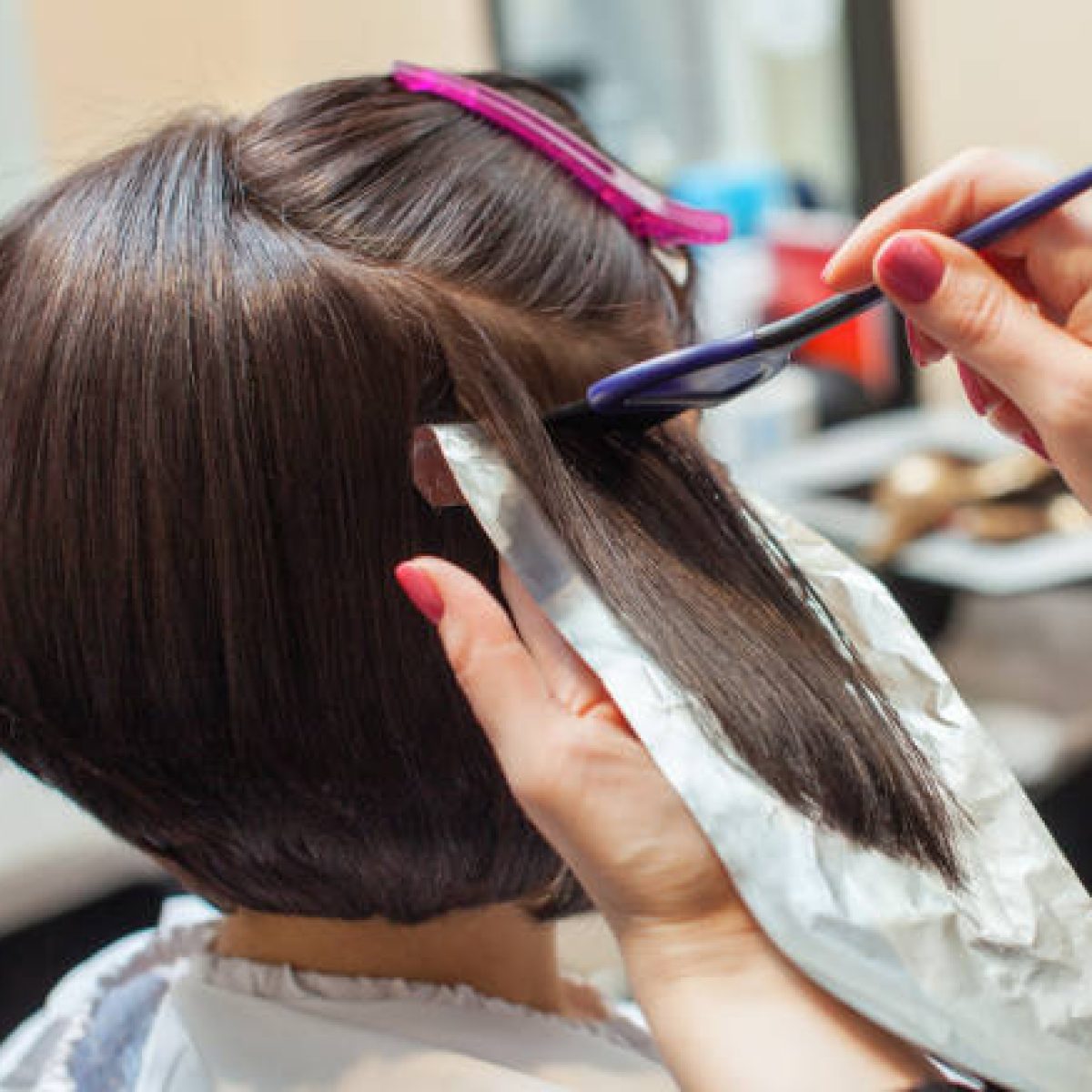 The hairdresser paints the woman's hair in a dark color, apply the paint to her hair in the beauty salon.